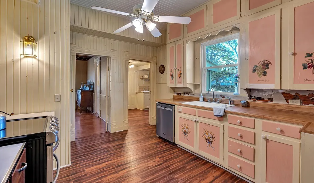 Kitchen with appliances with stainless steel finishes, dark wood-type flooring, ceiling fan, wood walls, and cream cabinetry