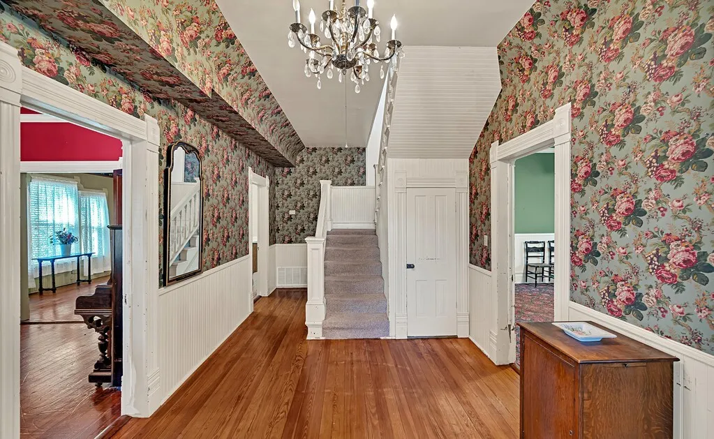 Hall featuring wallpapered walls, a chandelier, stairs, wood finished floors, and a wainscoted wall