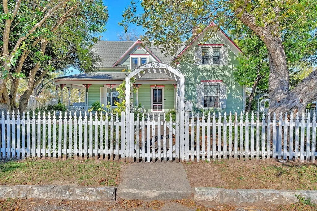 Victorian-style house featuring a gate, a porch, and a fenced front yard