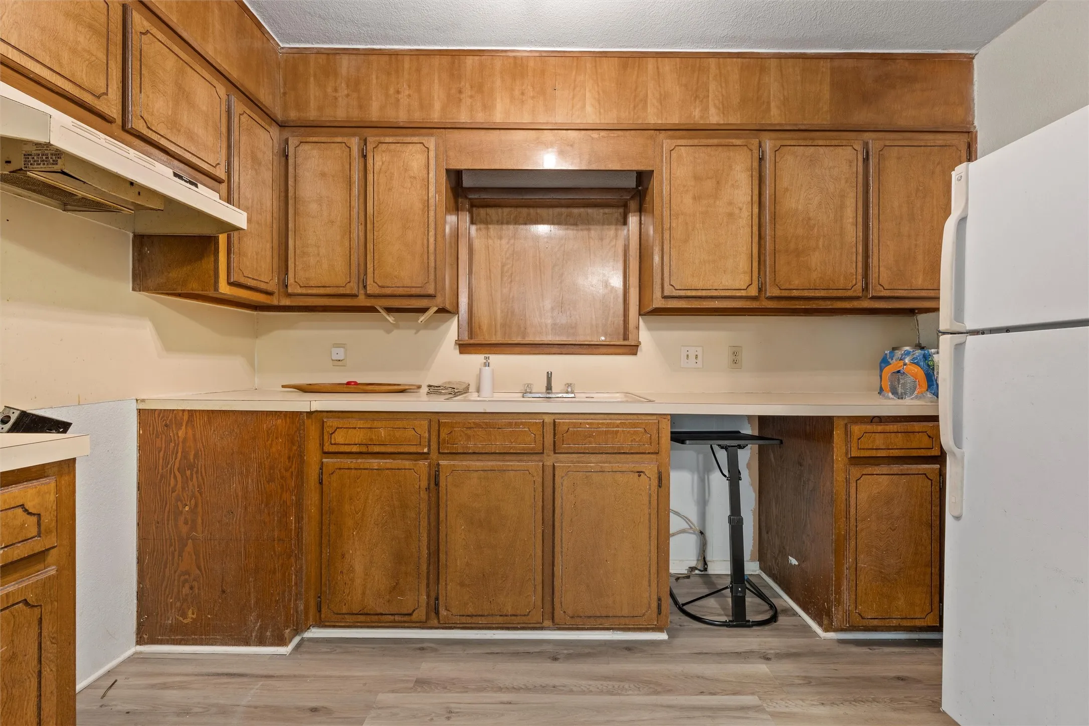 Kitchen featuring freestanding refrigerator, brown cabinets, and light countertops