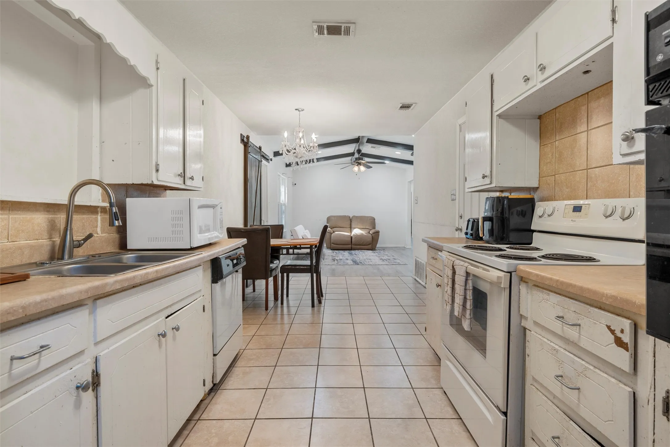 Kitchen with decorative backsplash, white appliances, light countertops, a barn door, and light tile patterned floors