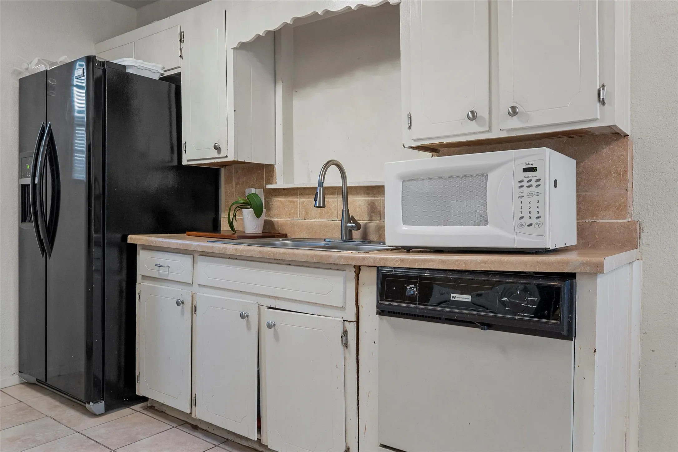 Kitchen featuring white appliances, light countertops, white cabinetry, light tile patterned floors, and decorative backsplash