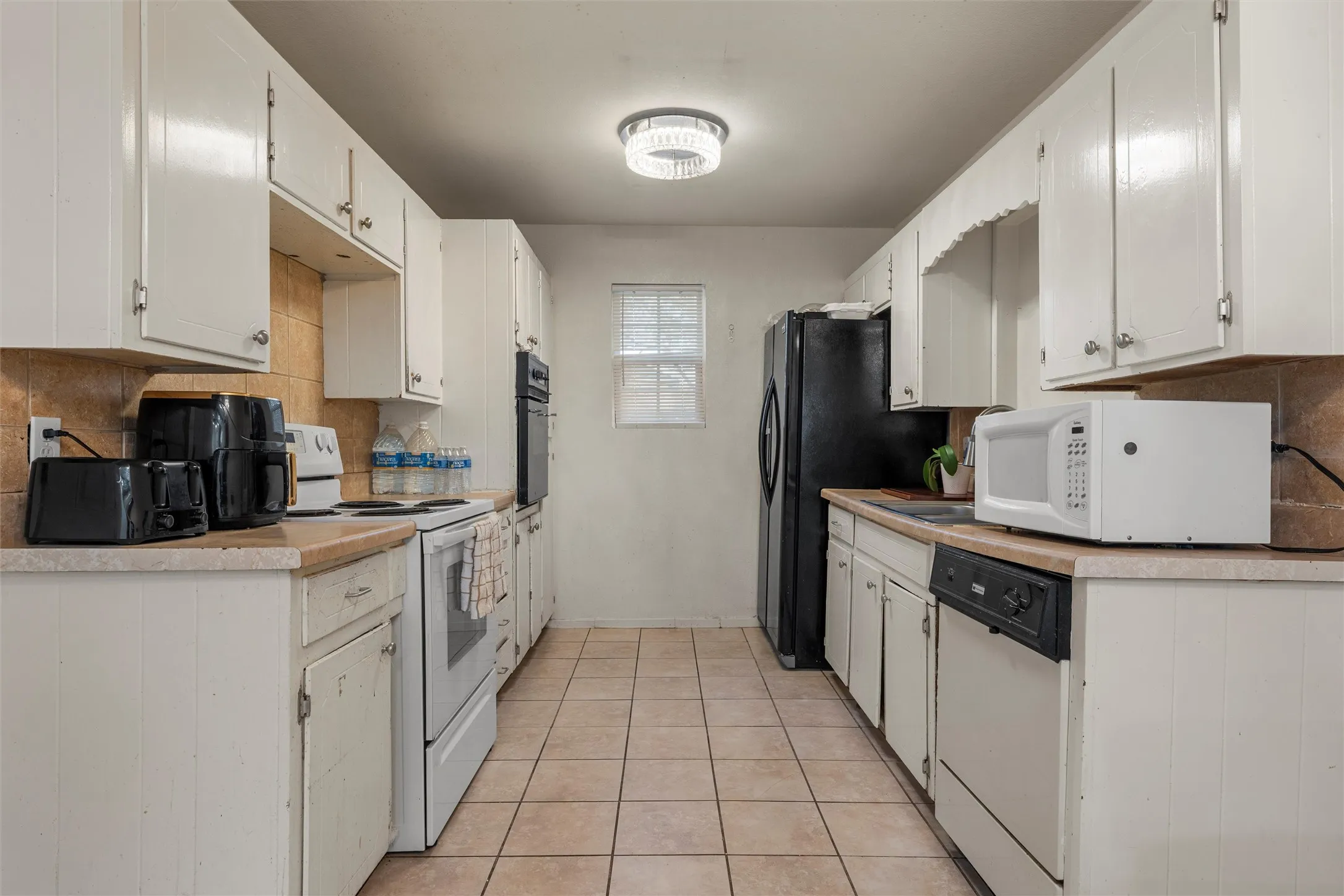 Kitchen featuring decorative backsplash, light countertops, light tile patterned flooring, white appliances, and white cabinetry