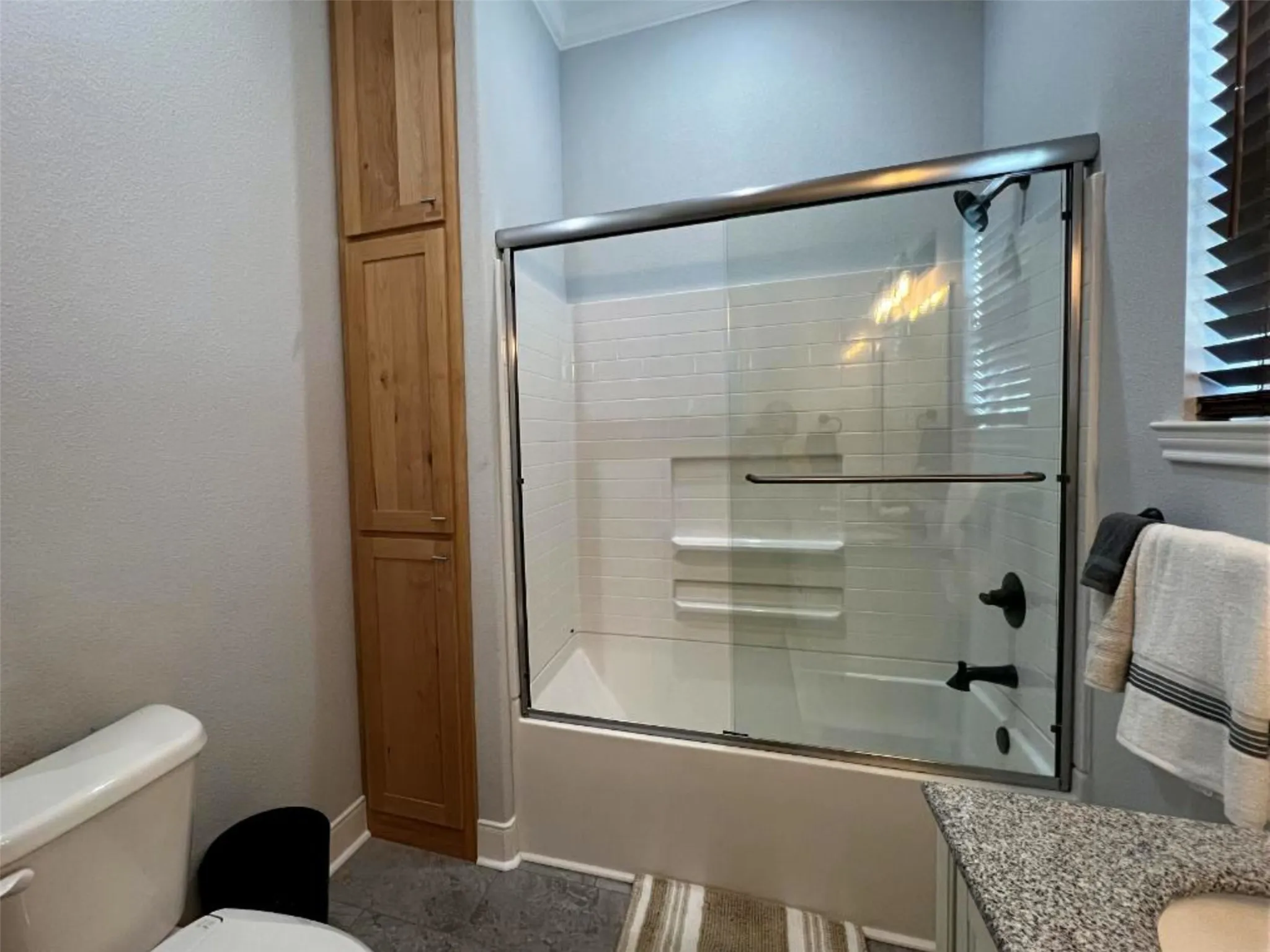 Bathroom featuring combined bath / shower with glass door, a textured wall, and vanity