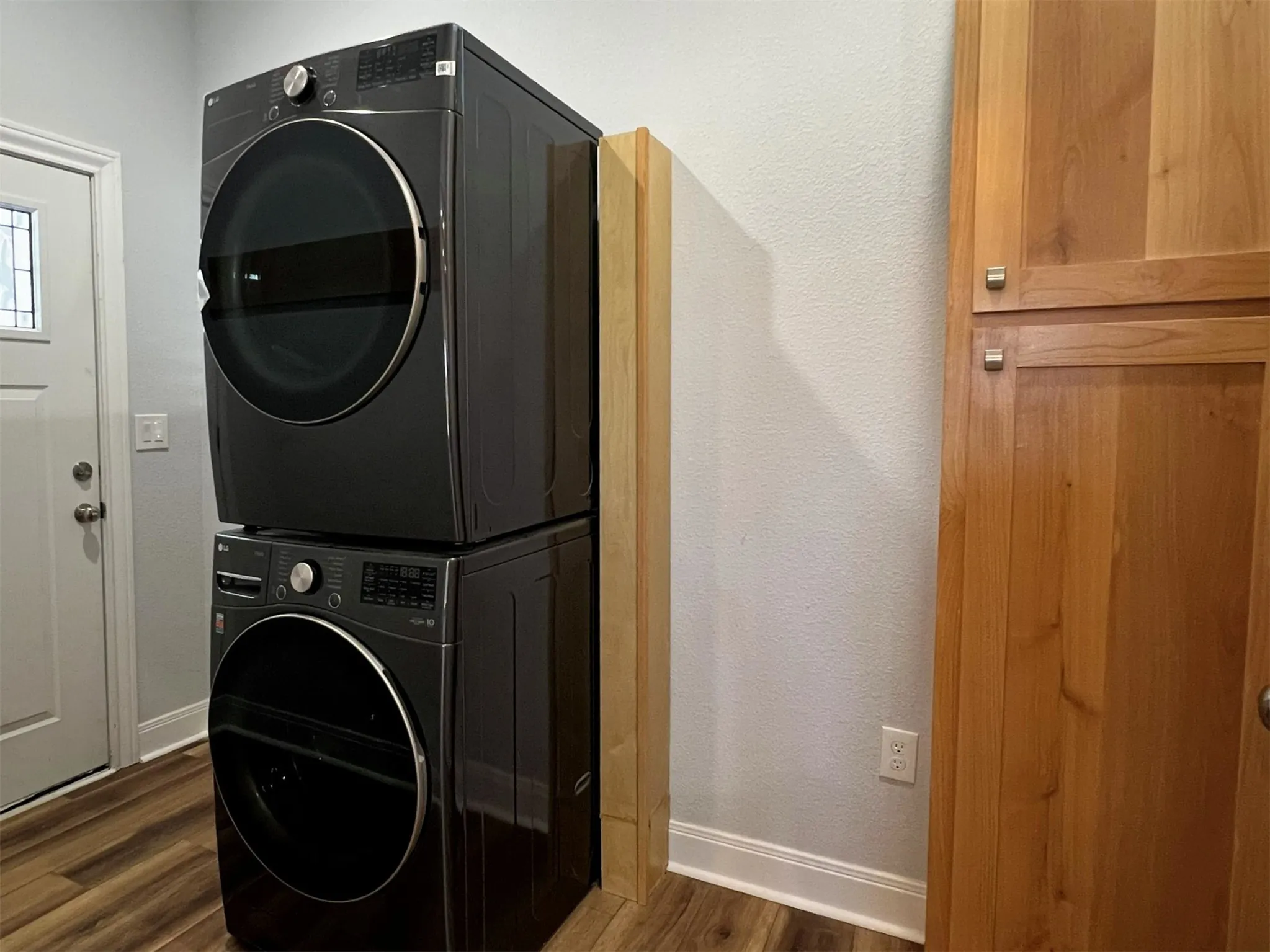 Laundry area featuring dark wood-style floors, estacked washer and dryer, and a textured wall