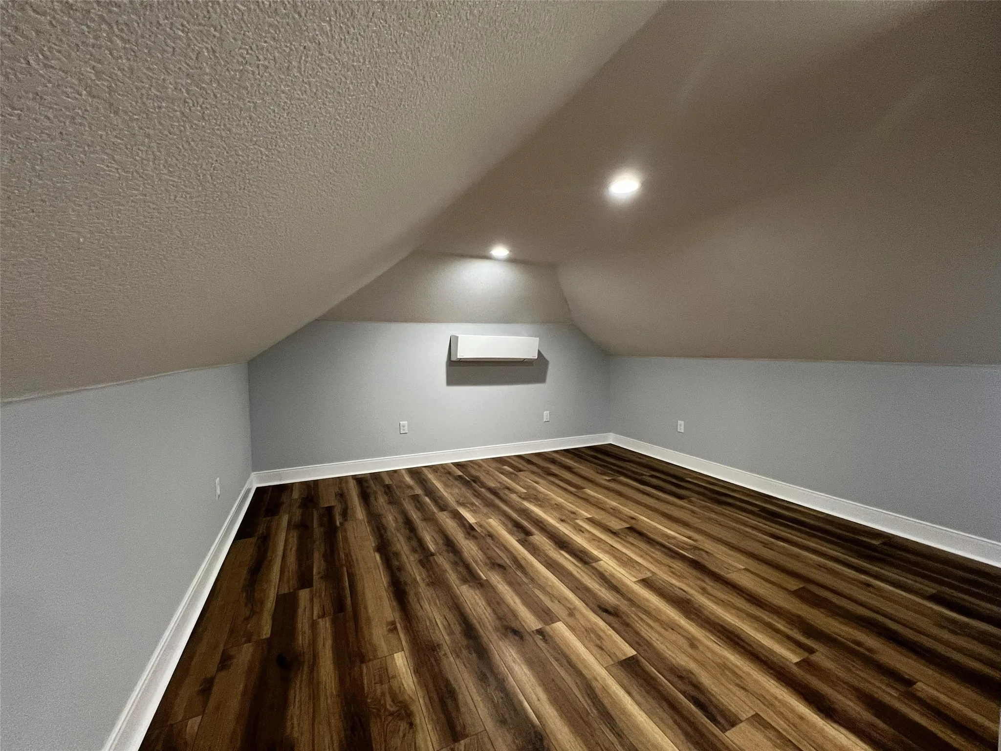 Bonus room with dark wood-type flooring, a textured ceiling, and lofted ceiling