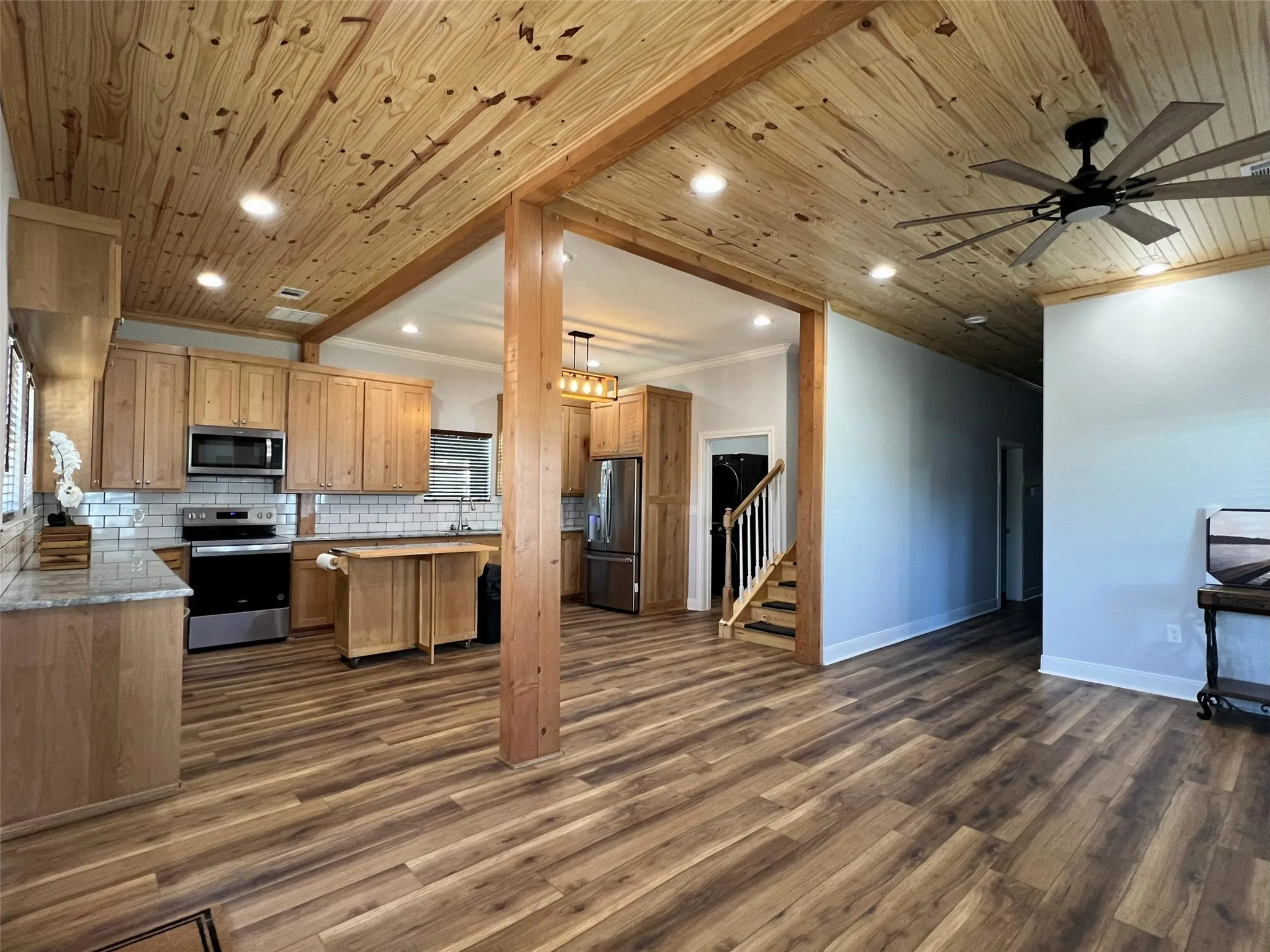 Kitchen featuring tasteful backsplash, open floor plan, appliances with stainless steel finishes, dark wood-style floors, and crown molding