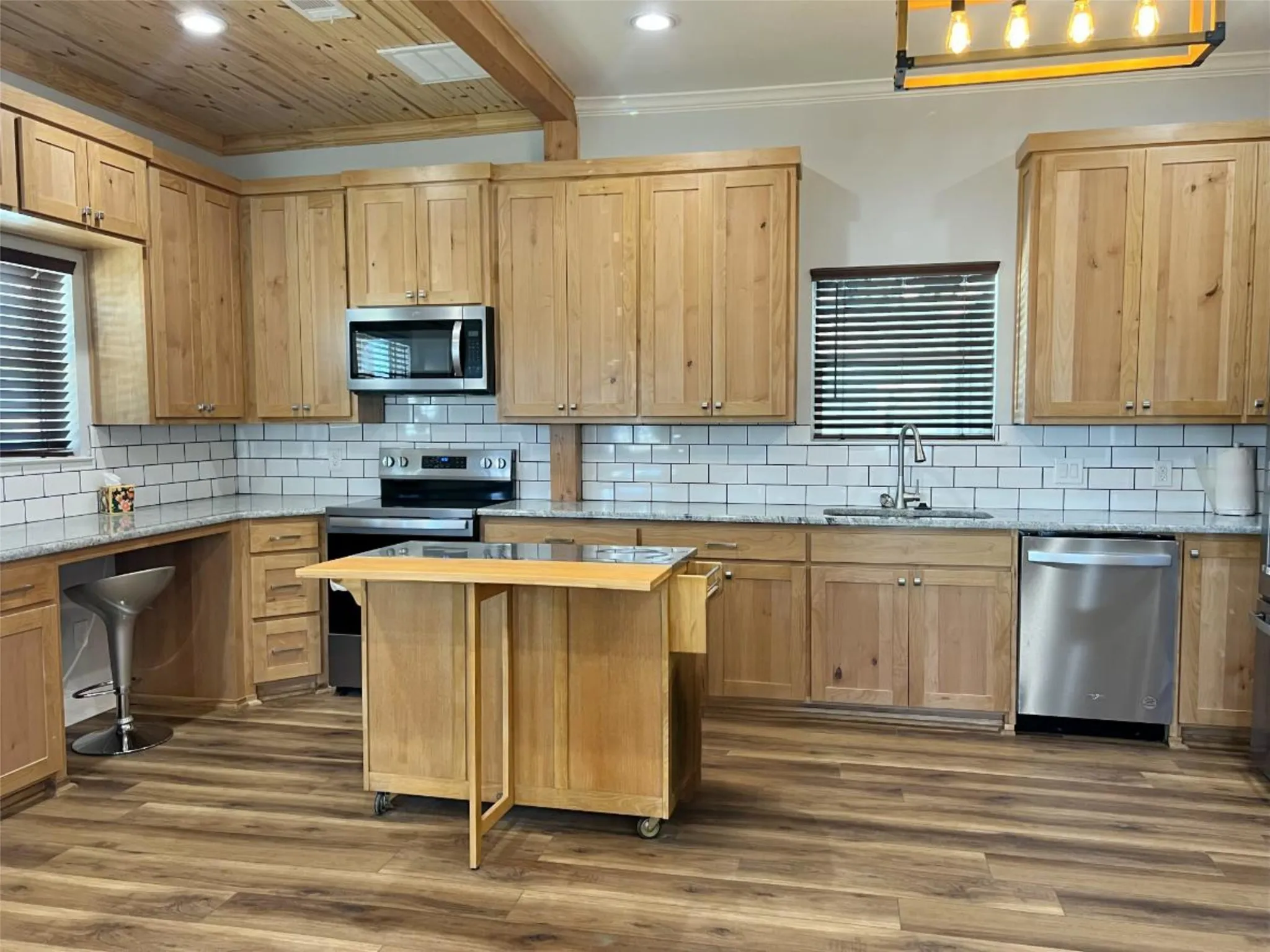 Kitchen featuring stainless steel appliances, light stone countertops, backsplash, beamed ceiling, and dark wood-type flooring