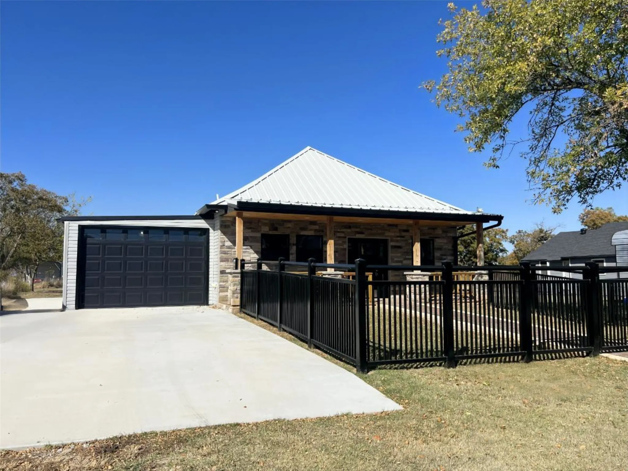 View of front of property with a fenced front yard, stone siding, driveway, a garage, and a metal roof