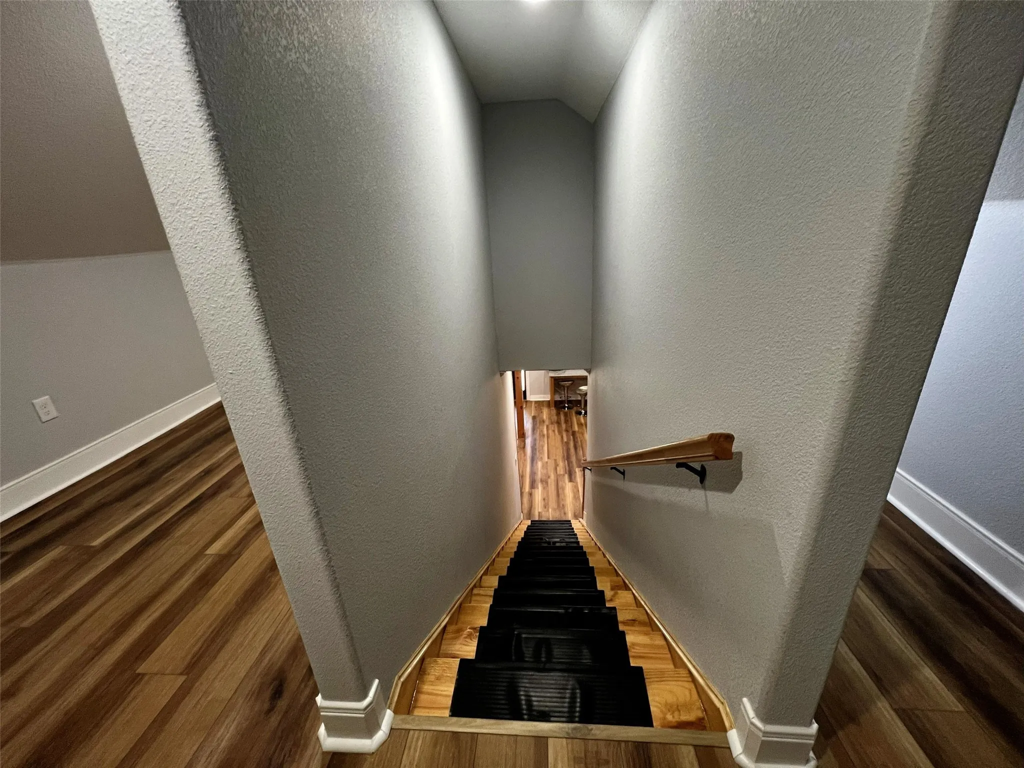 Staircase with wood finished floors, a textured wall, and lofted ceiling