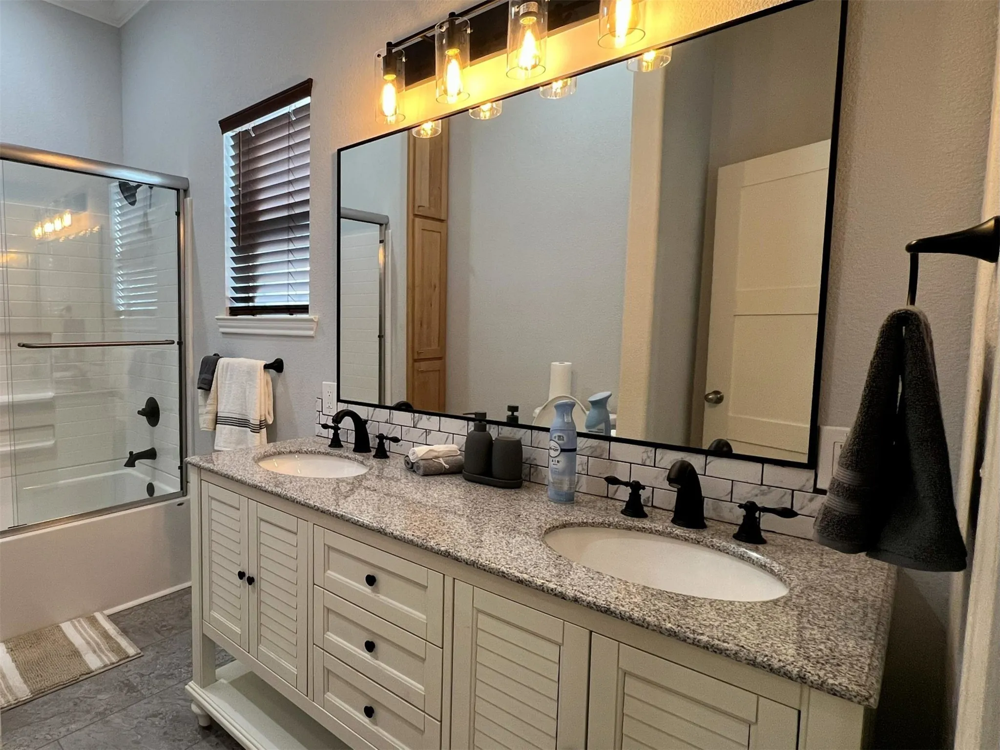 Full bathroom featuring double vanity, combined bath / shower with glass door, and decorative backsplash