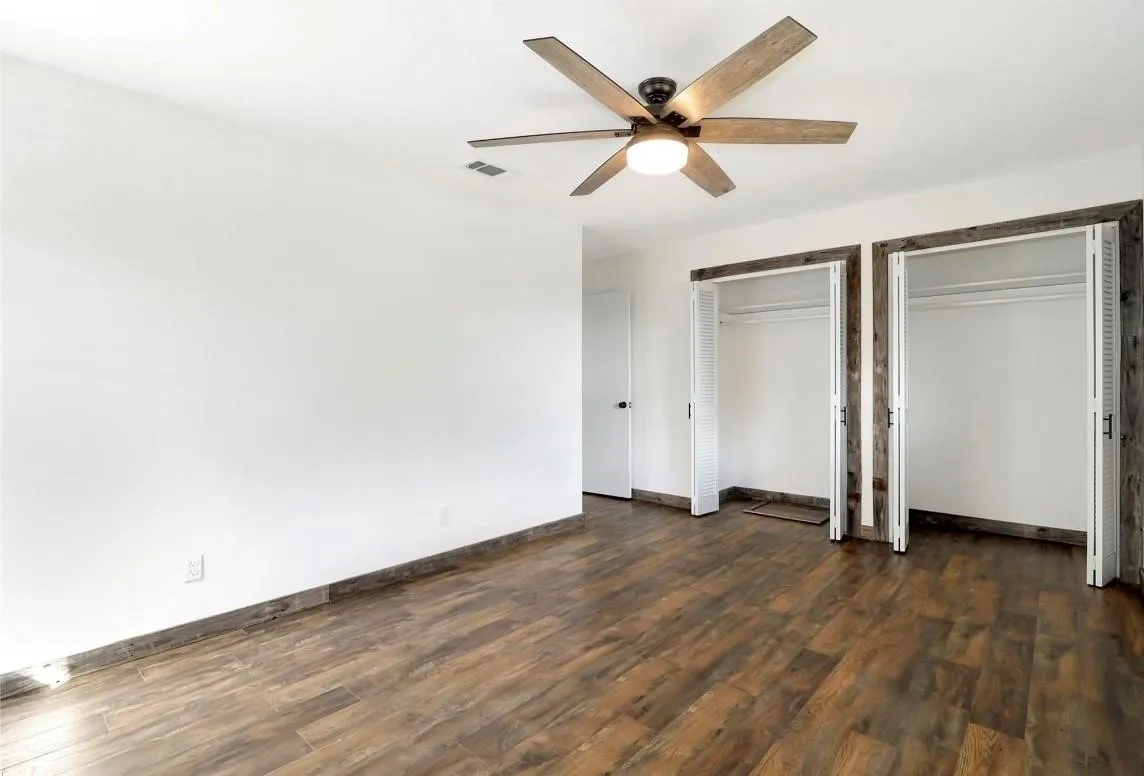 Unfurnished bedroom with multiple closets, dark wood finished floors, and ceiling fan