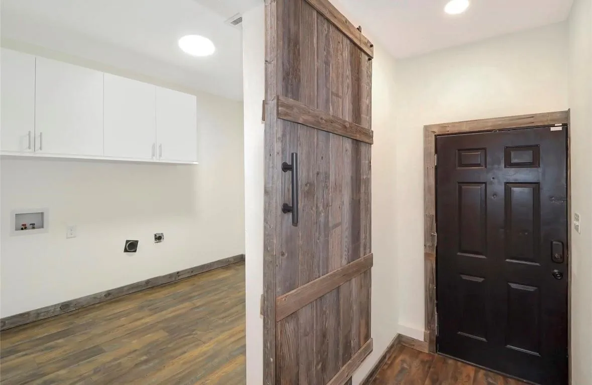 Laundry area featuring a barn door, dark wood finished floors, electric dryer hookup, cabinet space, and recessed lighting
