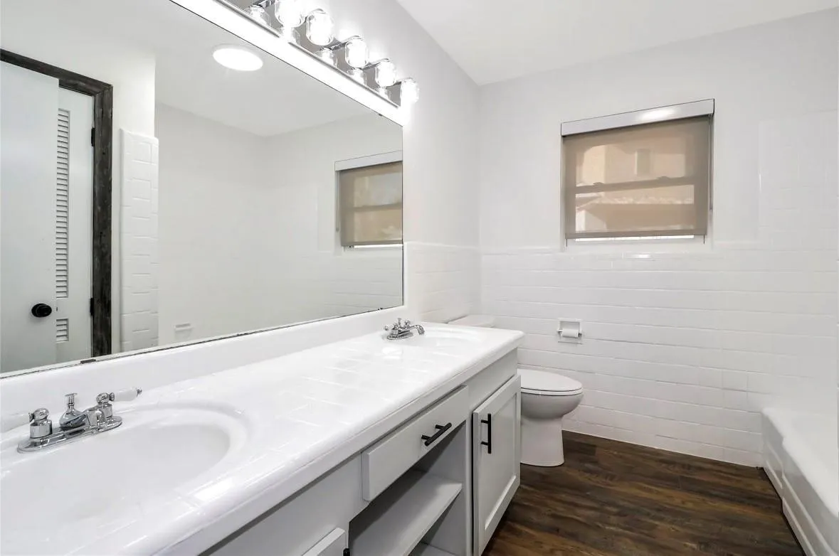 Bathroom featuring tile walls, dark wood-style flooring, double vanity, and wainscoting