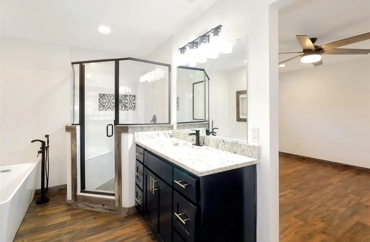 Bathroom featuring dark wood-style flooring, vanity, a freestanding tub, a stall shower, and ceiling fan