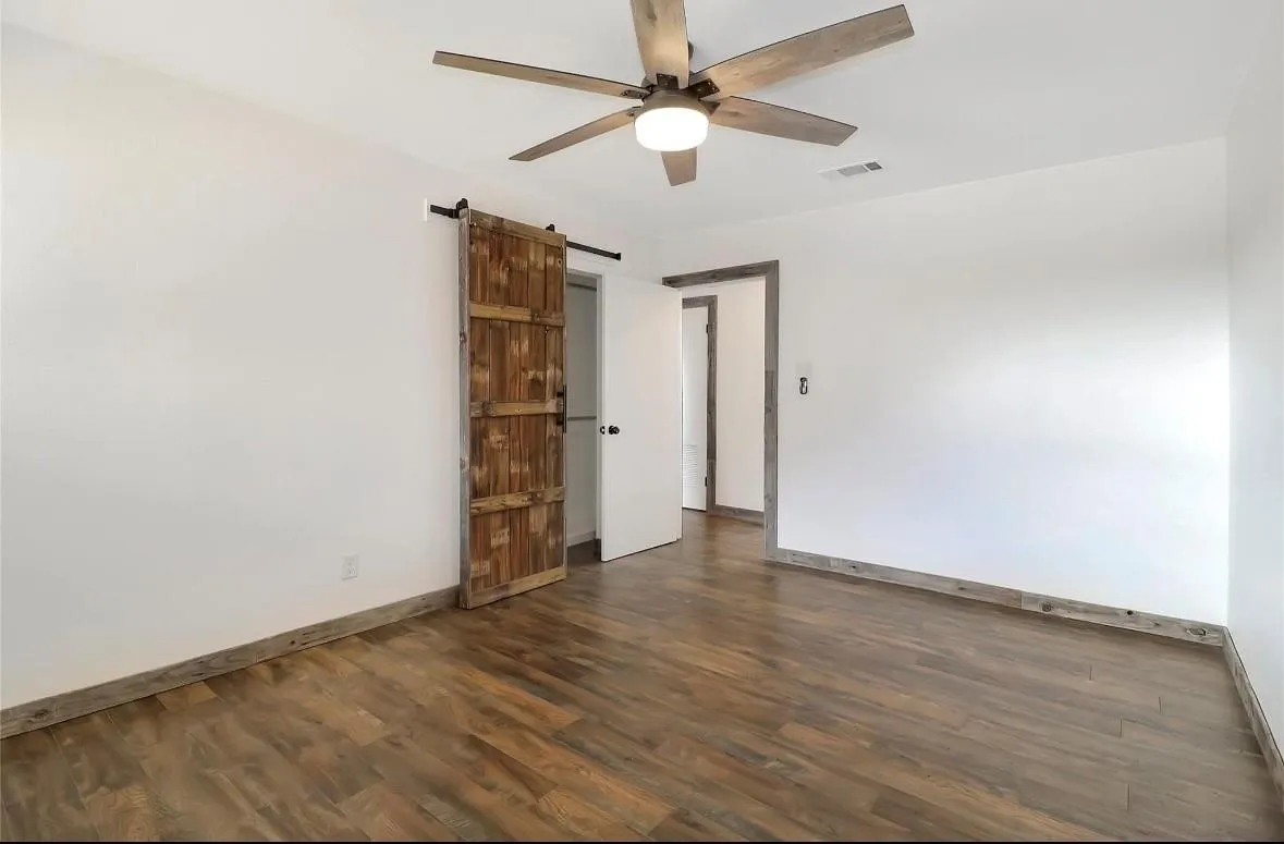 Spare room featuring a barn door, dark wood-type flooring, and ceiling fan