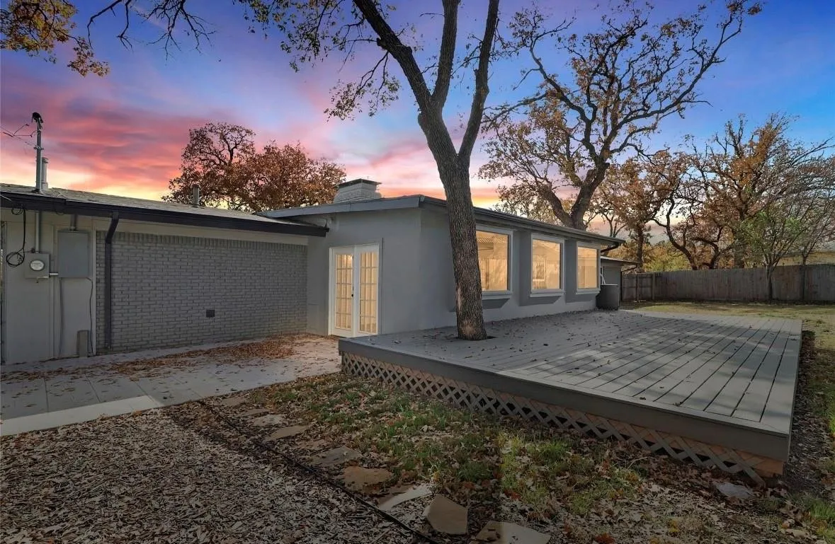 Back of house at dusk with a deck, a chimney, stucco siding, and brick siding