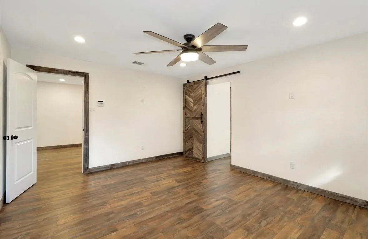 Unfurnished room featuring dark wood finished floors, a barn door, recessed lighting, and ceiling fan