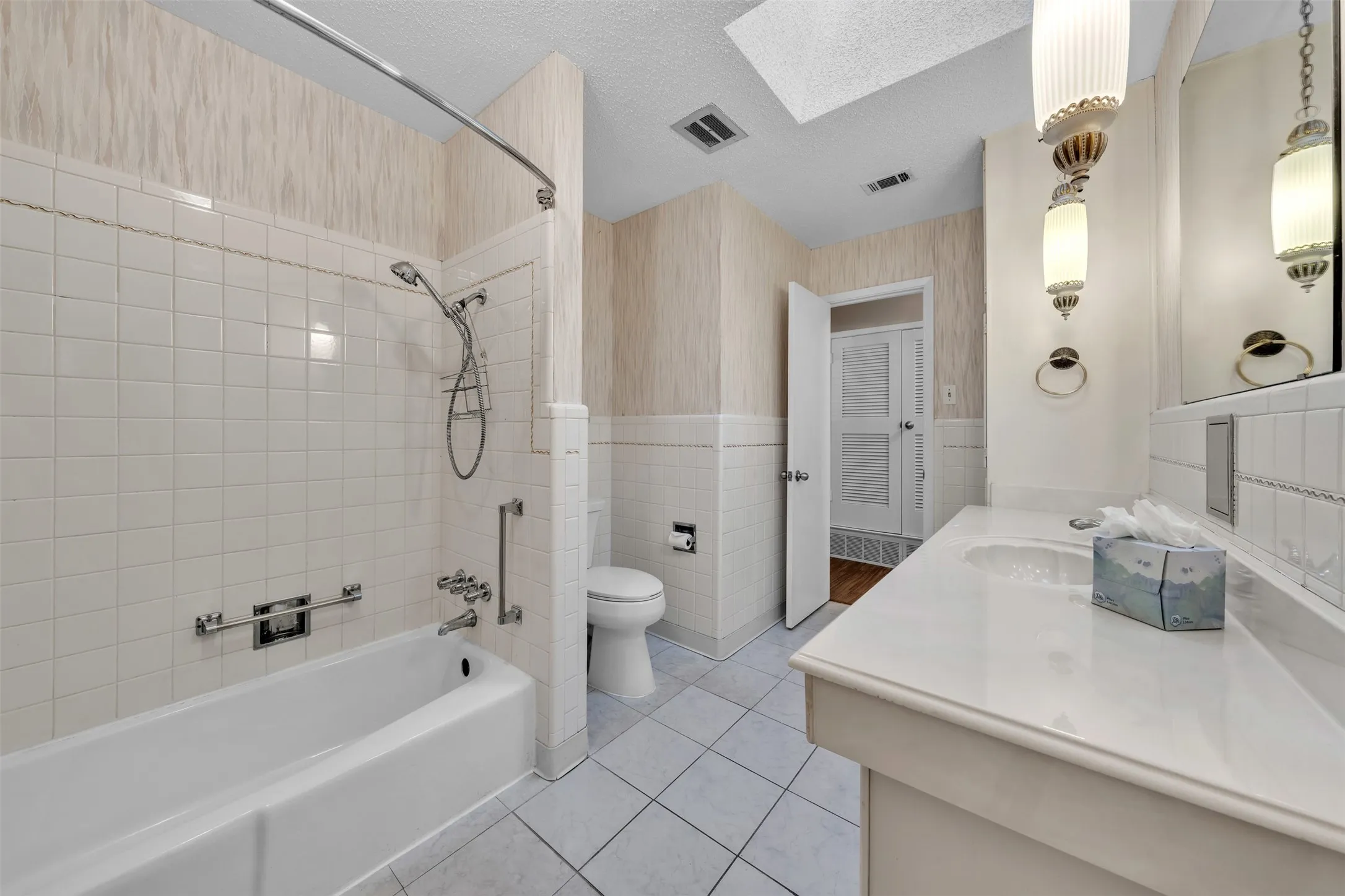 Full bath featuring bathing tub / shower combination, vanity, a skylight, light tile patterned floors, and a textured ceiling