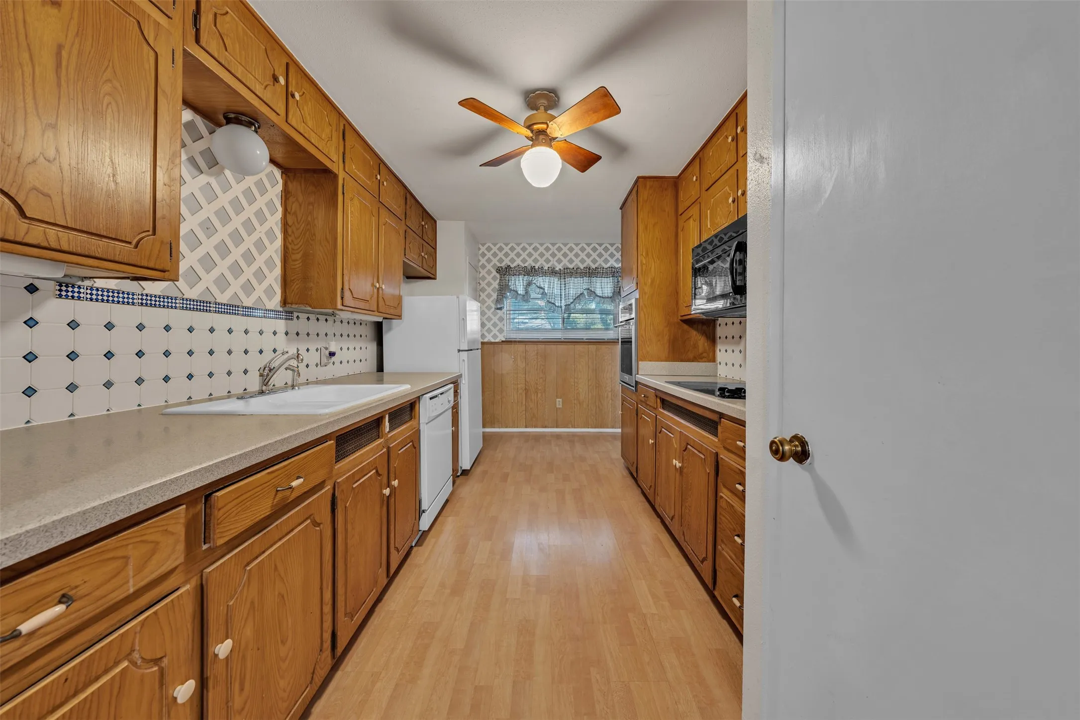 Kitchen featuring brown cabinetry, tasteful backsplash, white appliances, light wood-style flooring, and ceiling fan