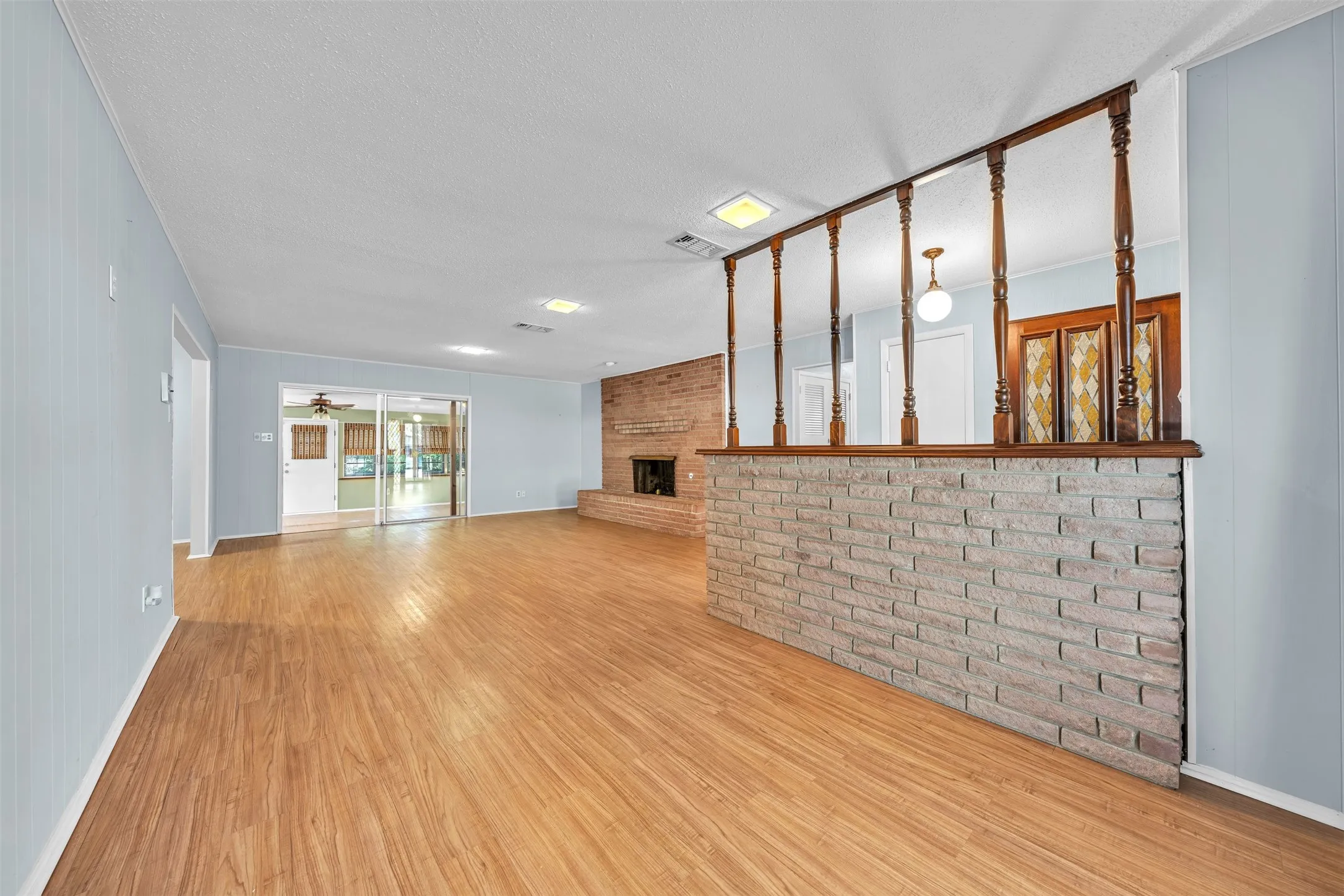 Unfurnished living room with brick wall, wood finished floors, a fireplace, a textured ceiling, and ceiling fan