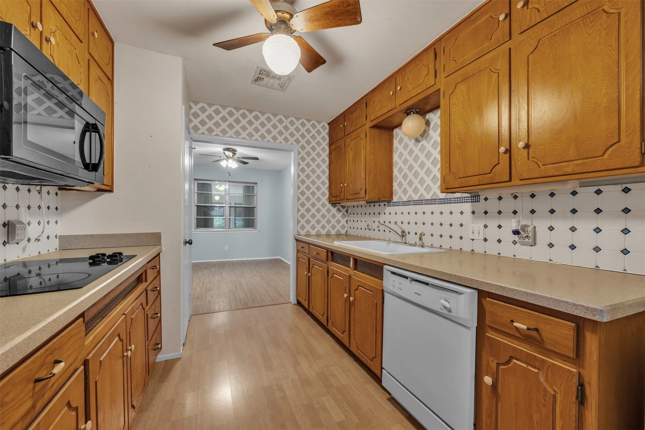 Kitchen featuring black appliances, brown cabinetry, light wood-type flooring, decorative backsplash, and a ceiling fan