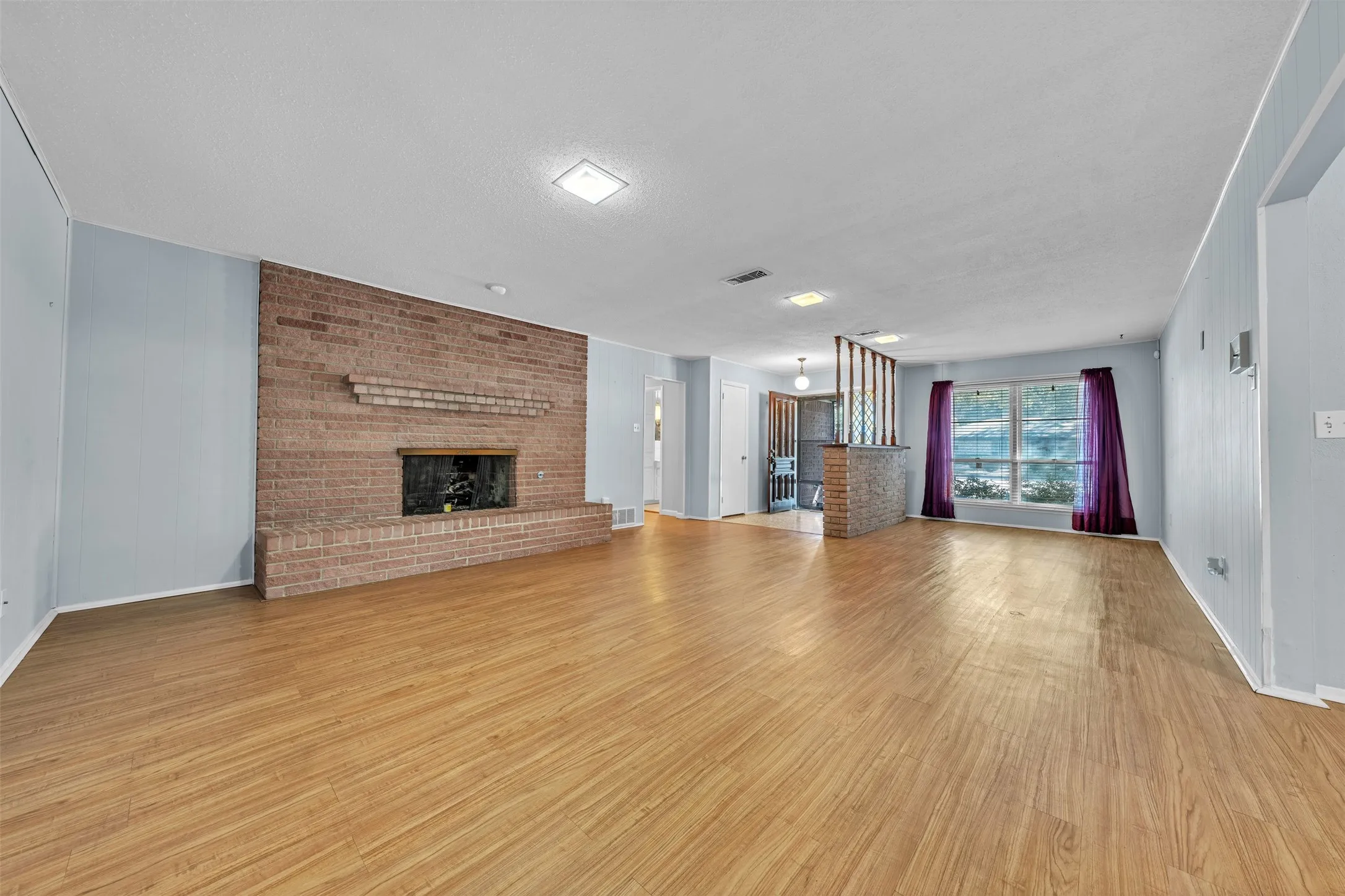 Unfurnished living room featuring a fireplace, light wood-type flooring, wooden walls, and a textured ceiling