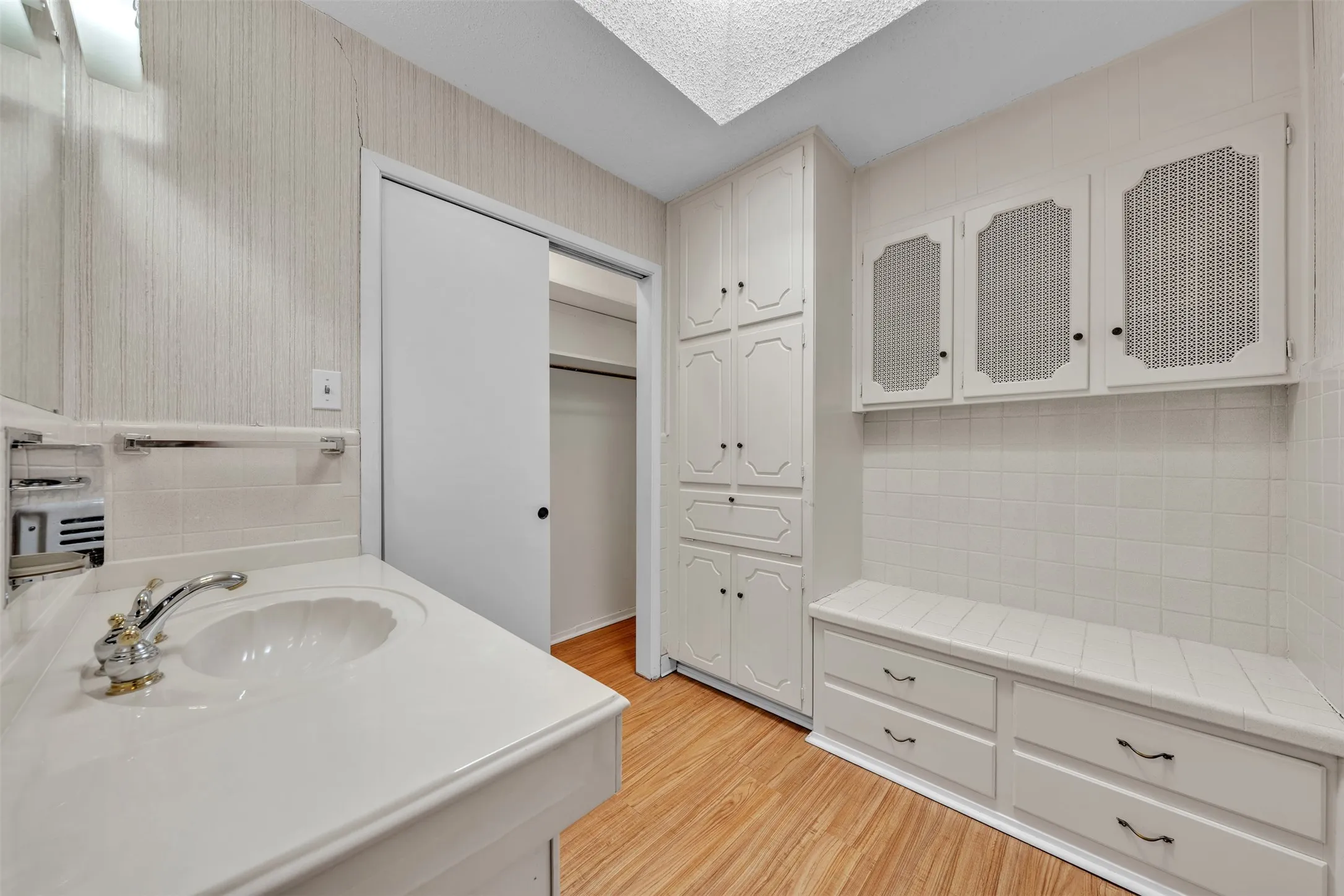 Bathroom featuring vanity, light wood-type flooring, a spacious closet, decorative backsplash, and wallpapered walls
