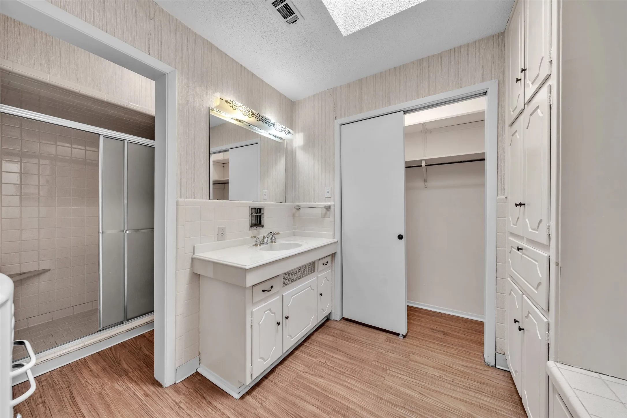 Full bath with wallpapered walls, vanity, a textured ceiling, a skylight, and light wood-style floors