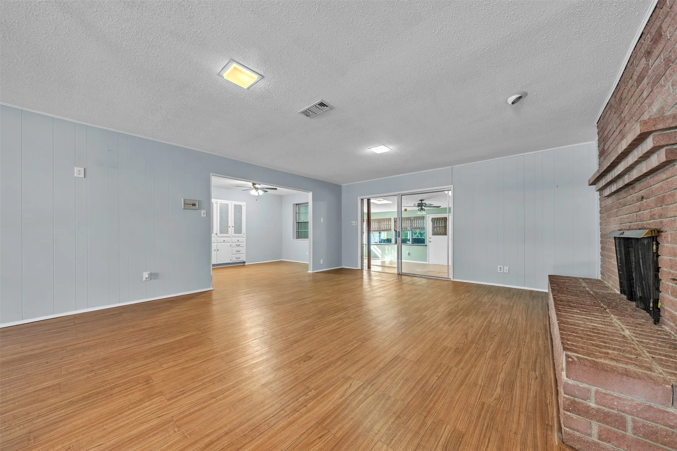 Unfurnished living room with wood walls, light wood-style floors, a textured ceiling, a fireplace, and ceiling fan