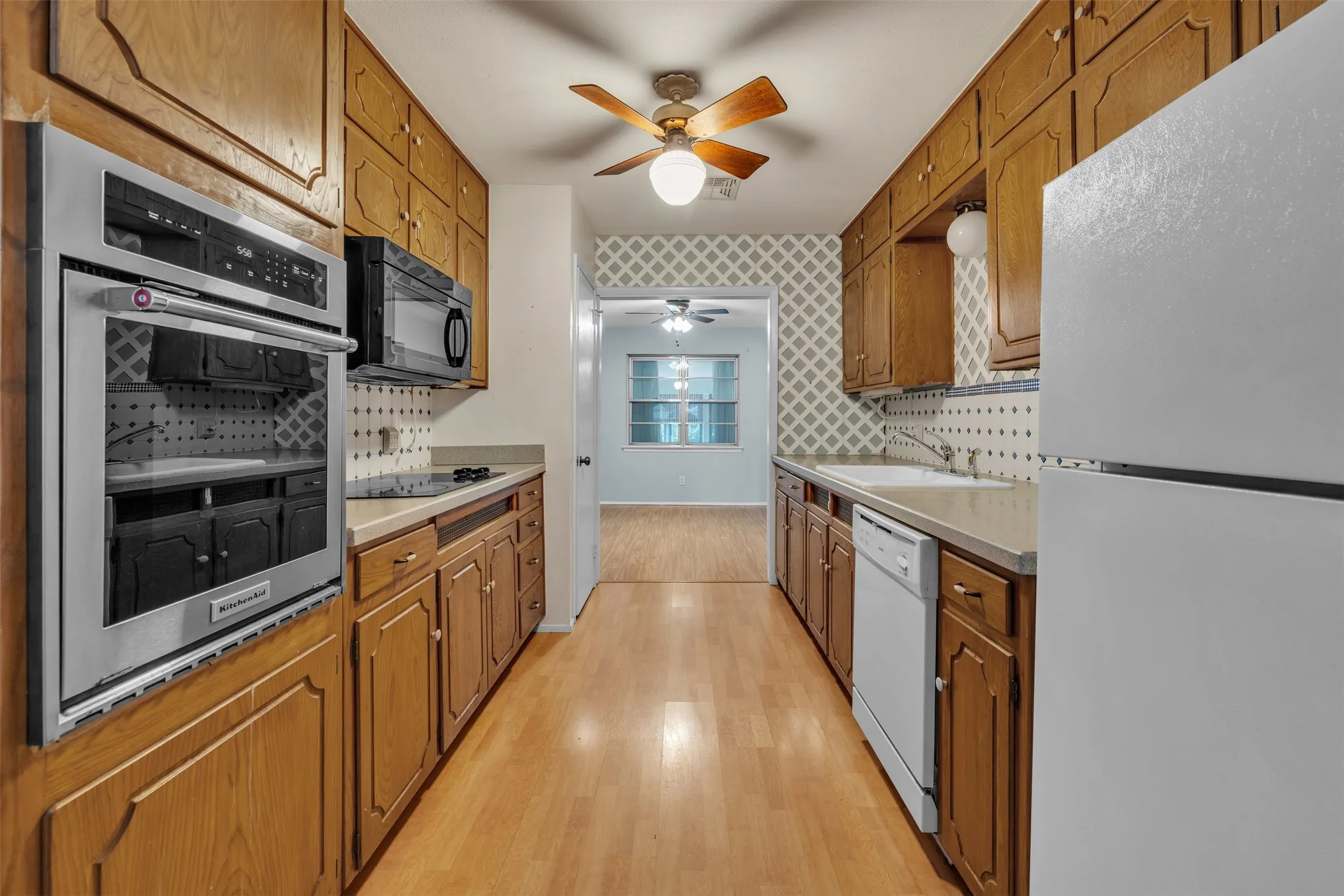 Kitchen featuring black appliances, brown cabinets, light wood-type flooring, and wallpapered walls