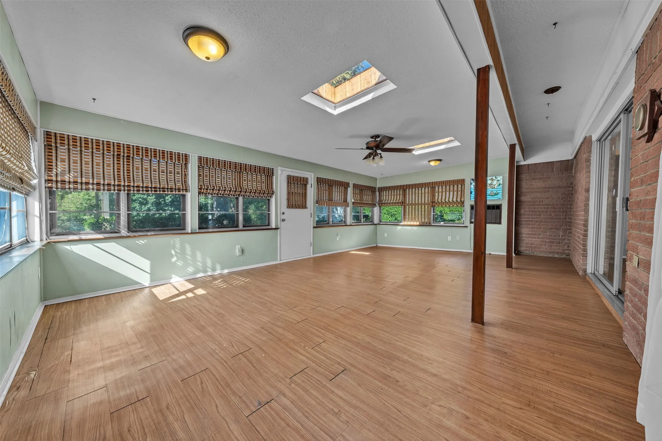 Unfurnished sunroom featuring brick wall, a skylight, and wood finished floors