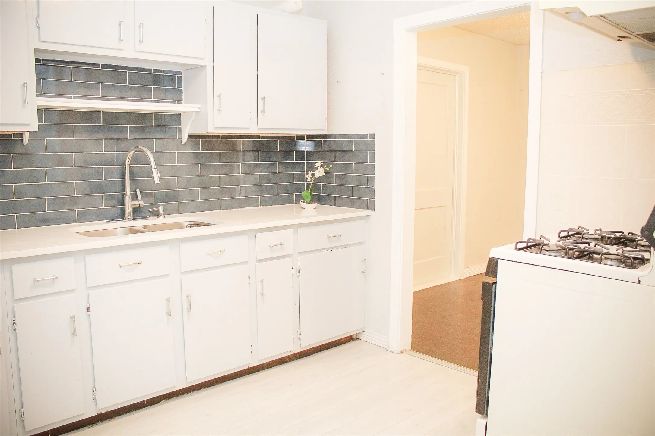 Kitchen featuring white gas stove, tasteful backsplash, white cabinets, ventilation hood, and light wood-style flooring