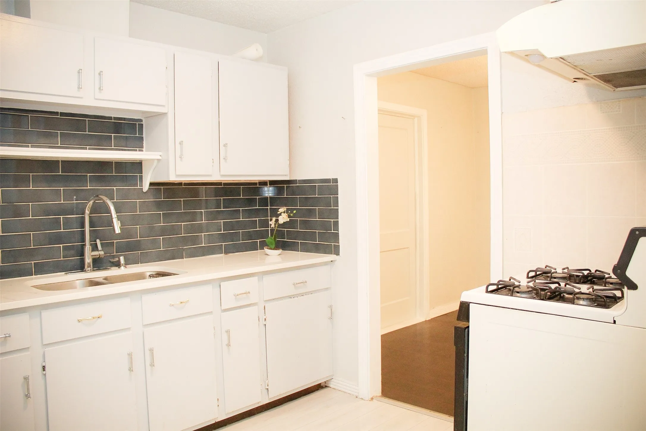 Kitchen featuring white gas stove, ventilation hood, white cabinetry, decorative backsplash, and light wood-type flooring