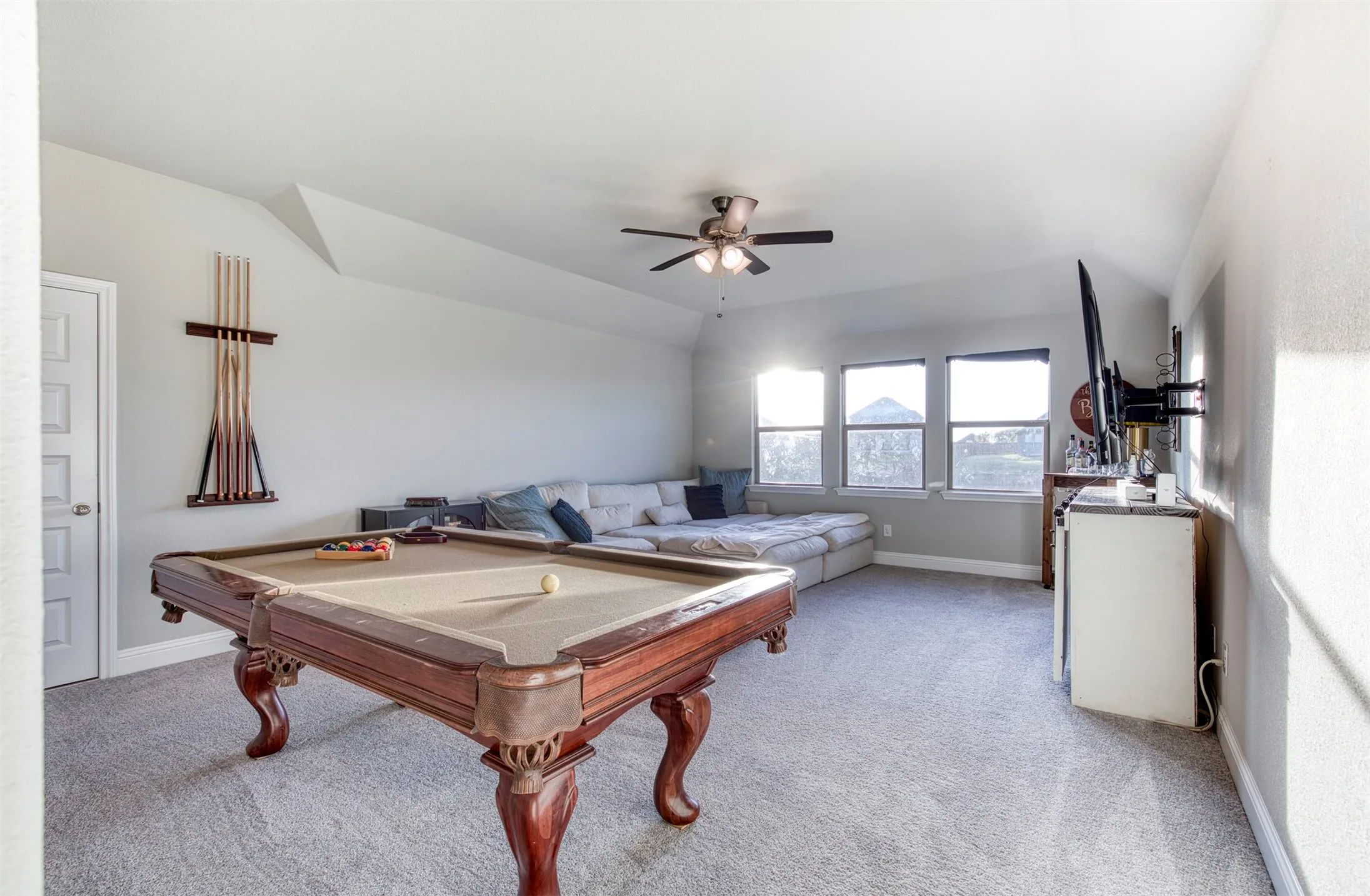 Game room with ceiling fan and wall of windows for natural light.