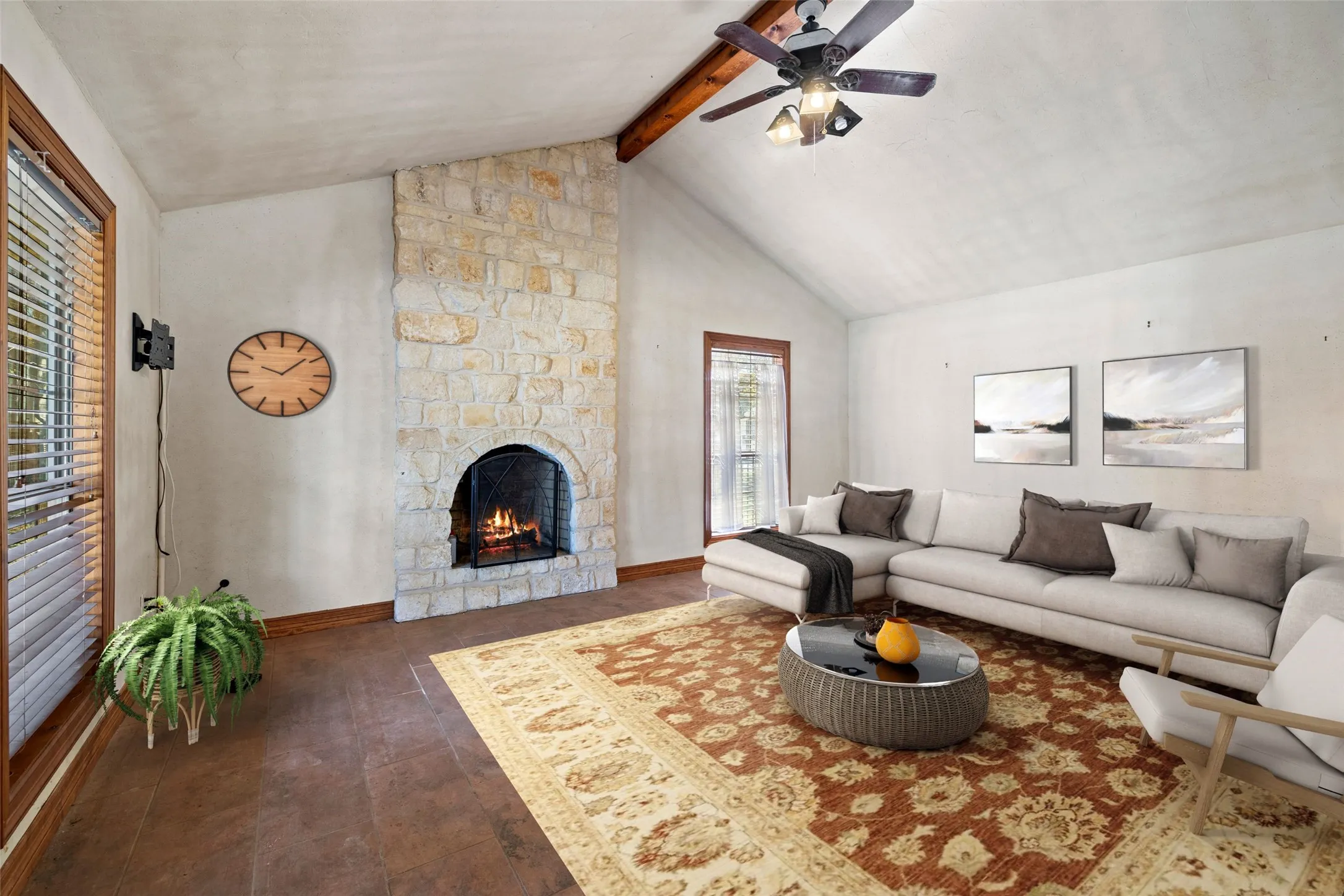 Living room featuring beam ceiling, a stone fireplace, high vaulted ceiling, a ceiling fan, and wood finished floors
