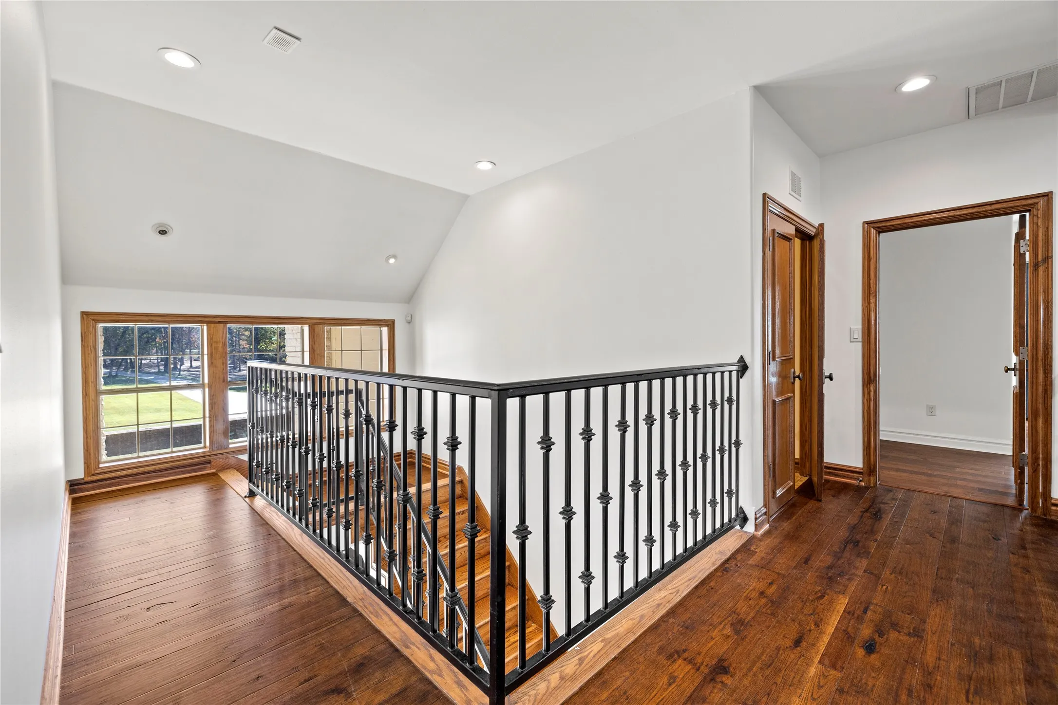 Corridor with dark wood-style floors, recessed lighting, vaulted ceiling, and an upstairs landing