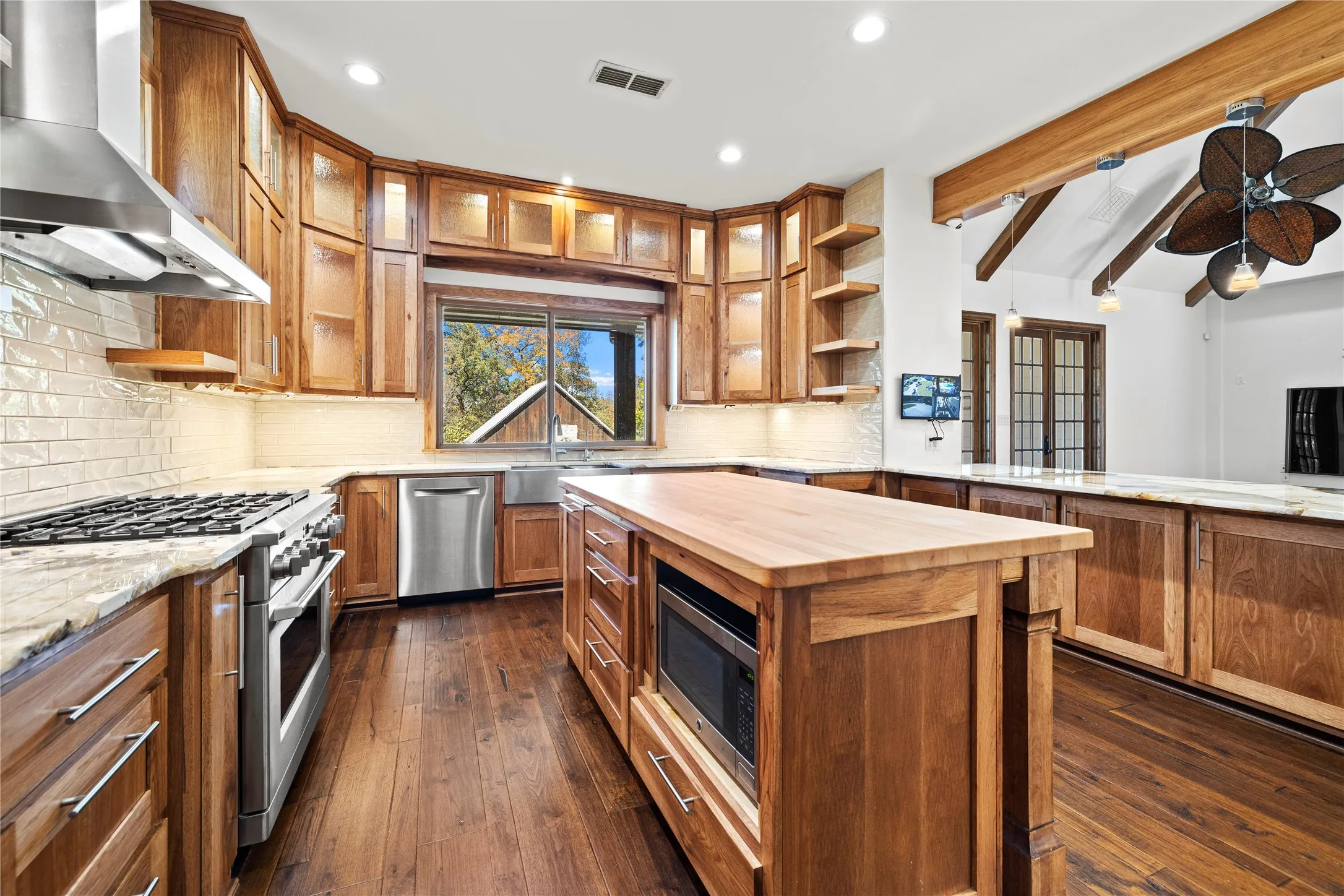 Kitchen with open shelves, beam ceiling, wall chimney exhaust hood, wooden counters, and dark wood-style flooring
