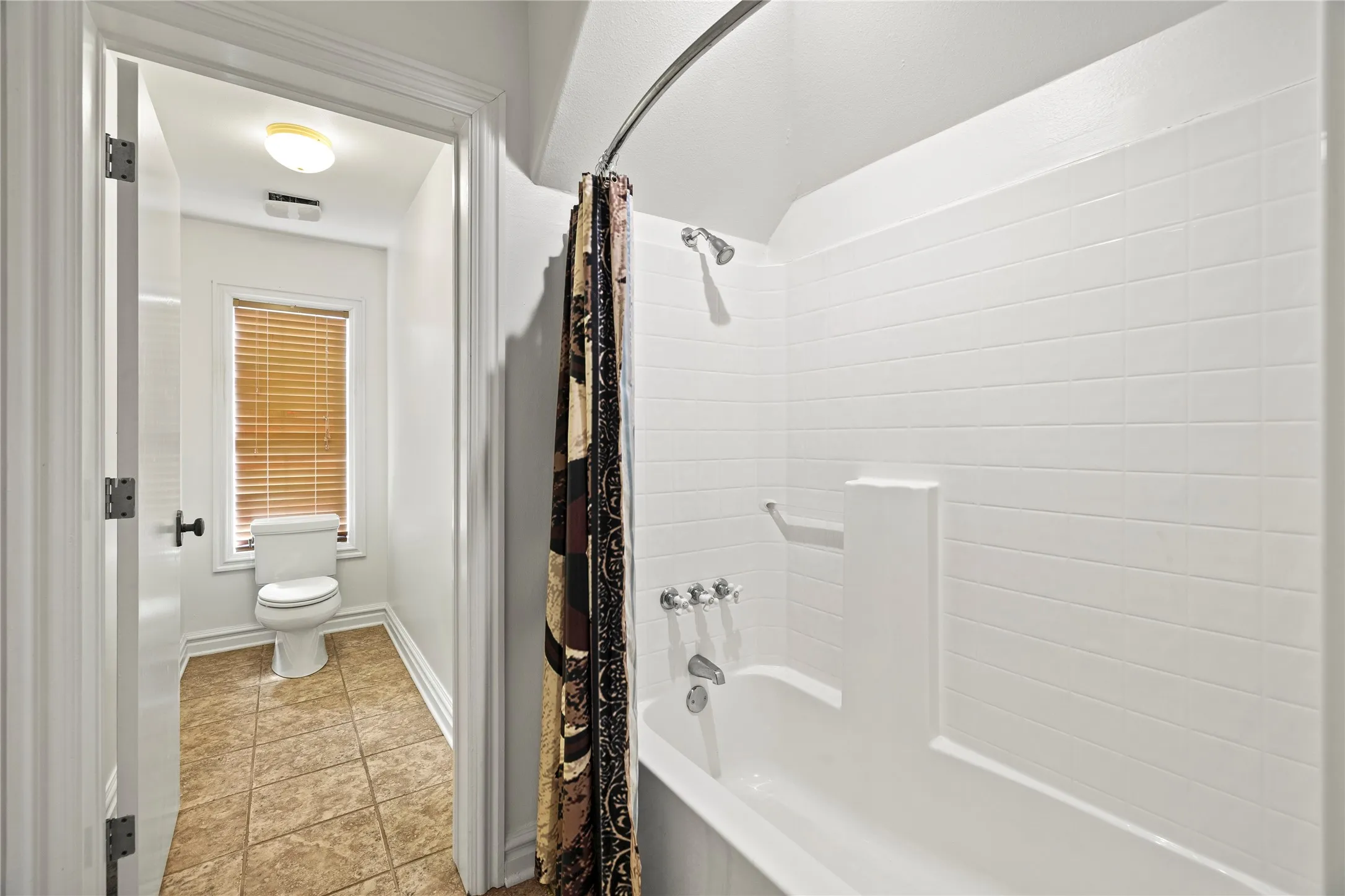 Bathroom with shower / bath combo with shower curtain and light tile patterned floors