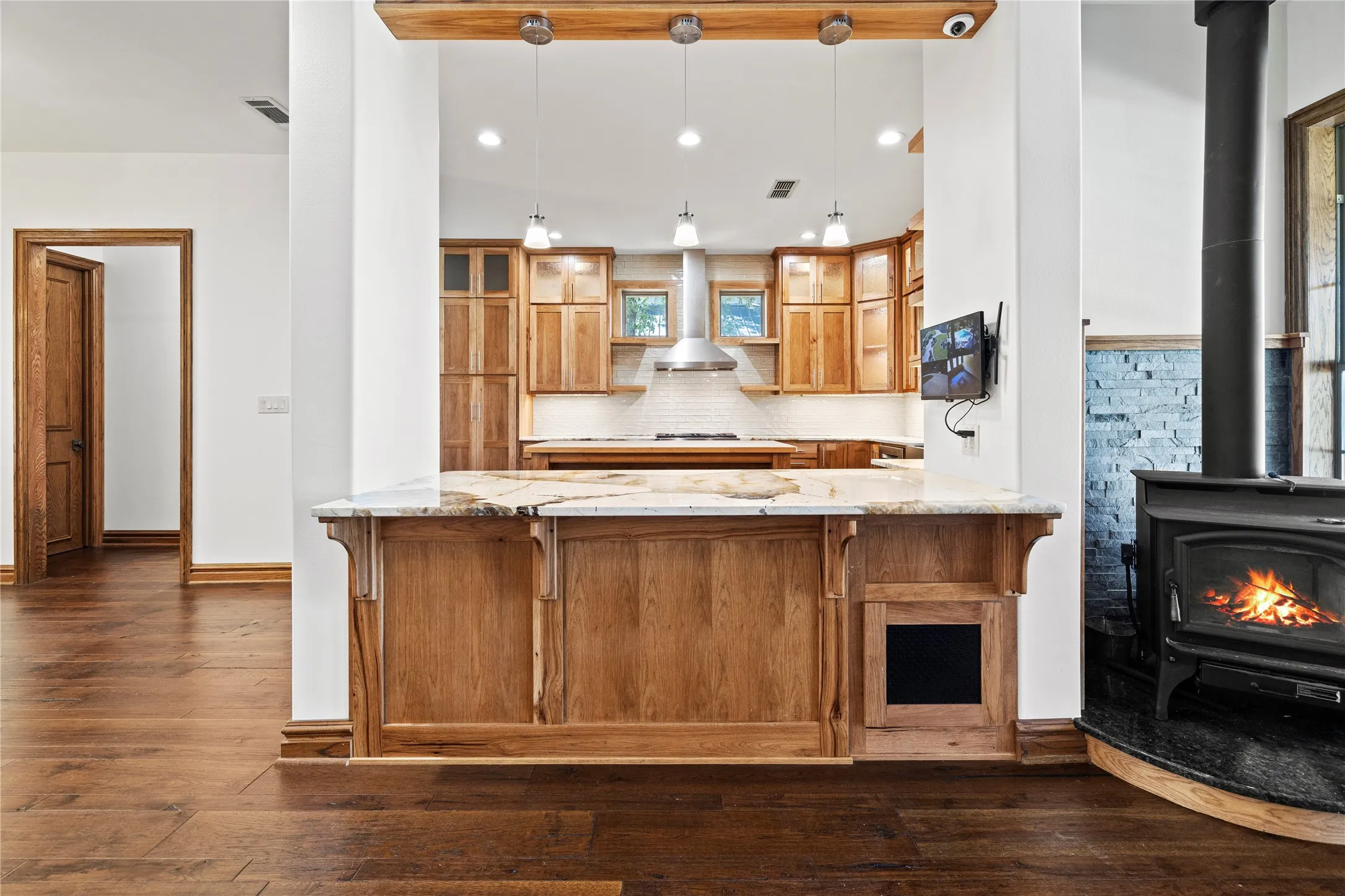 Kitchen featuring a wood stove, a kitchen bar, recessed lighting, dark wood-style flooring, and pendant lighting
