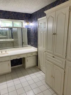Bathroom featuring tile patterned floors, vanity for ease of putting on makeup, a textured ceiling, and wallpapered walls.