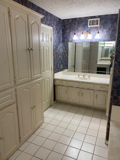 Bathroom with vanity, wallpapered walls, tile patterned floors, a textured ceiling, and visible vents.