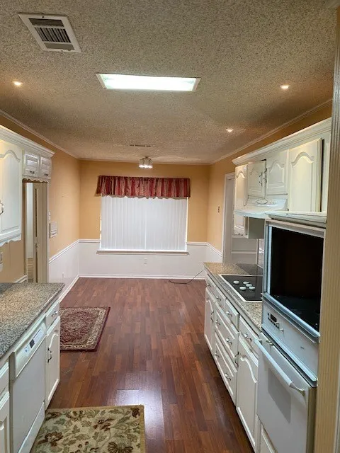 Kitchen with visible vents, a textured ceiling, oven, and wainscoting