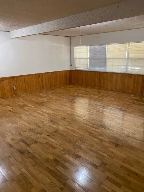 Spare  living room with hardwood / wood-style floors, wood walls, a textured ceiling, and a wainscoted wall