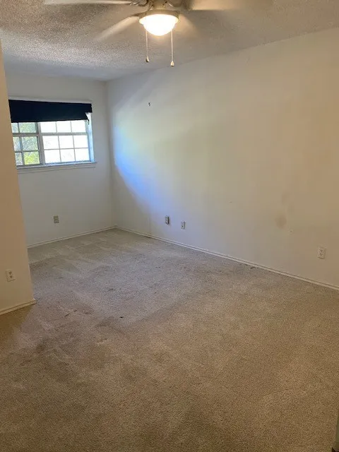 Unfurnished bedroom featuring a textured ceiling, light colored carpet, baseboards, and a ceiling fan