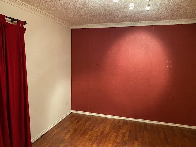 Empty dining room featuring crown molding, baseboards, wood finished floors, and a textured ceiling.