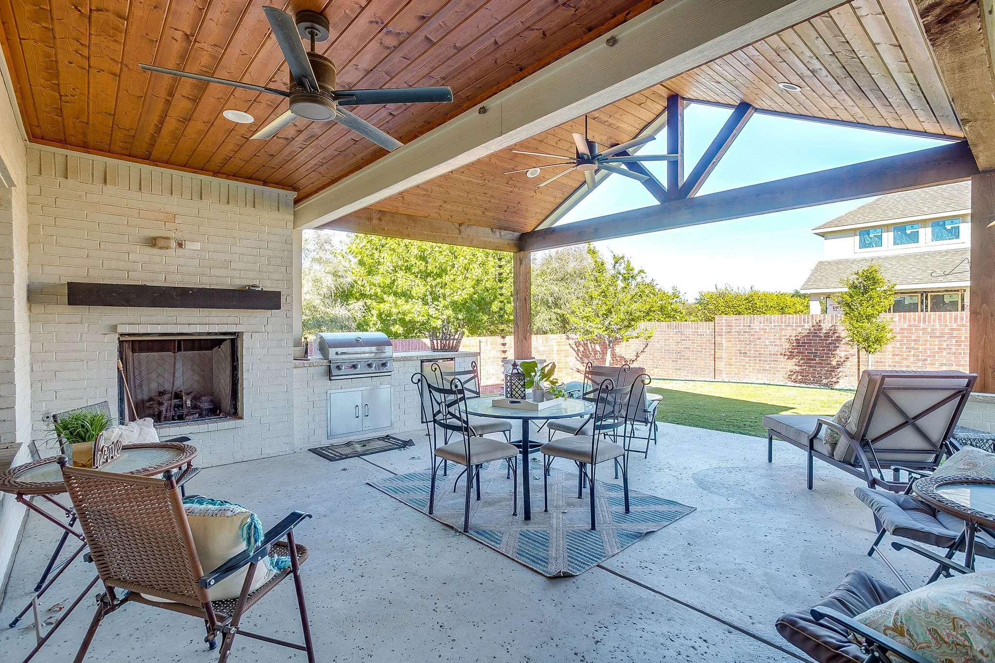 Fenced backyard featuring ceiling fan, an outdoor brick fireplace, a patio, outdoor dining area, and area for grilling