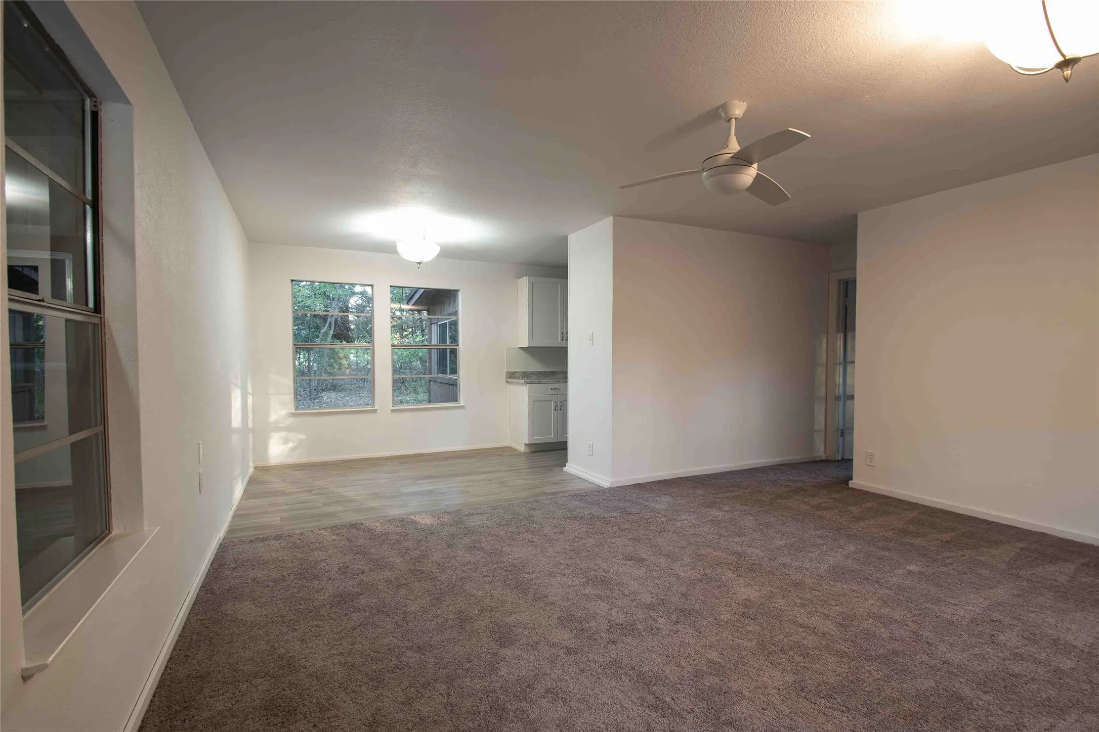 Unfurnished Living room and dining room featuring dark carpet, laminate flooring  and ceiling fan