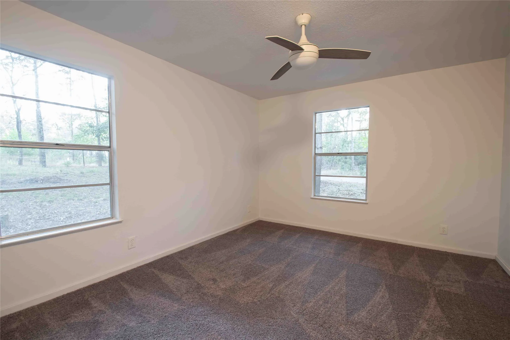 Primary bedroom featuring a textured ceiling, dark colored carpet, and ceiling fan