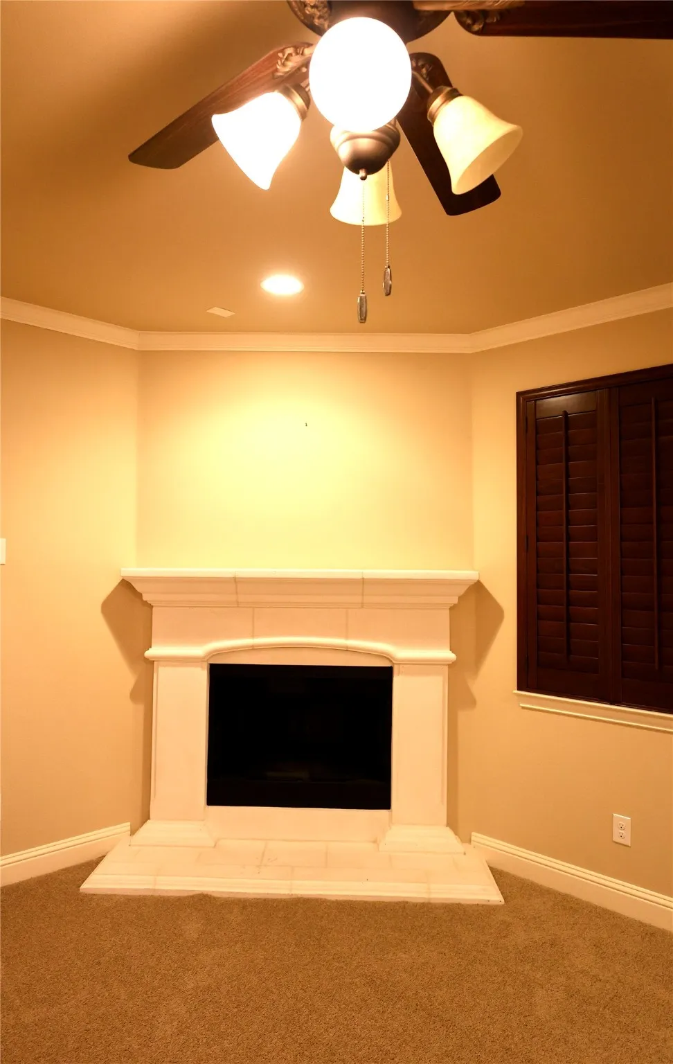 Detailed view of carpet floors, a fireplace with raised hearth, ceiling fan, crown molding, and recessed lighting